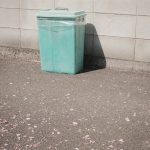 green plastic trash bin beside white wall