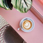 cup of coffee on saucer with teaspoon on pink tabletop